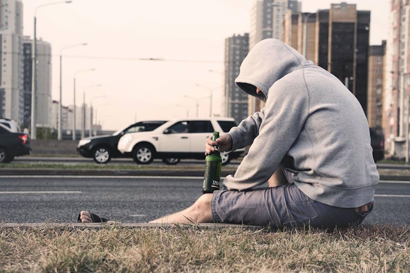  Man sitting alone on a roadside with a bottle in his hand, showing the emotional weight of romantic rejection
