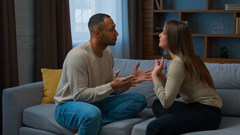 Couple sitting on the couch in a tense conversation, struggling with a repeated argument